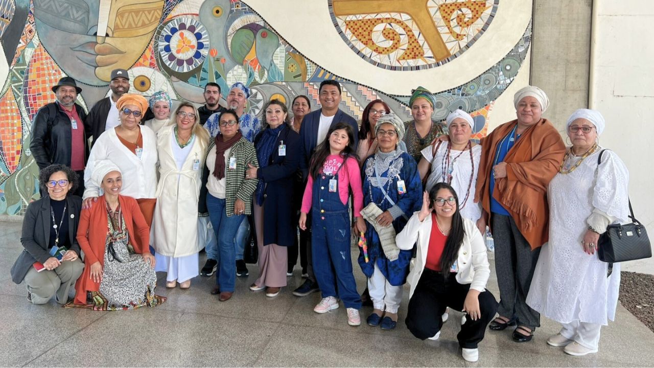 Diretor de Turismo, Yuri Benites, e a gerente de Turismo Sustentável, Silvana Gomes, acompanhados por integrantes da Comissão Organizadora da Festa de Iemanjá, em frente ao painel Ysy – A Mãe Água, no Itaipu Parquetec. Créditos: Itaipu Parquetec.
